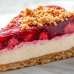 A slice of strawberry crunch cheesecake on a white marble countertop.